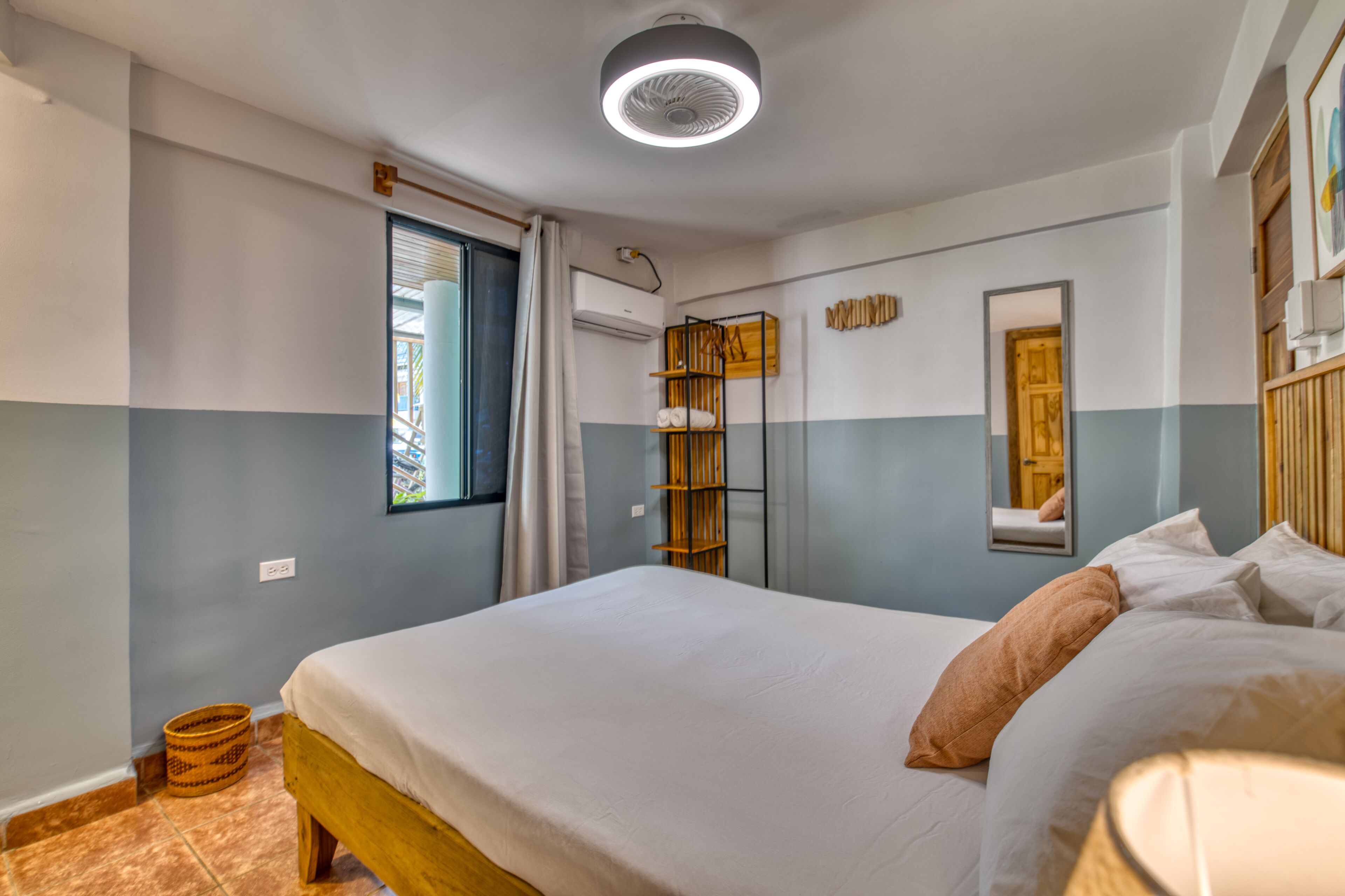 A bedroom with a bed, a bedside table, a mirror, and a window with curtains.