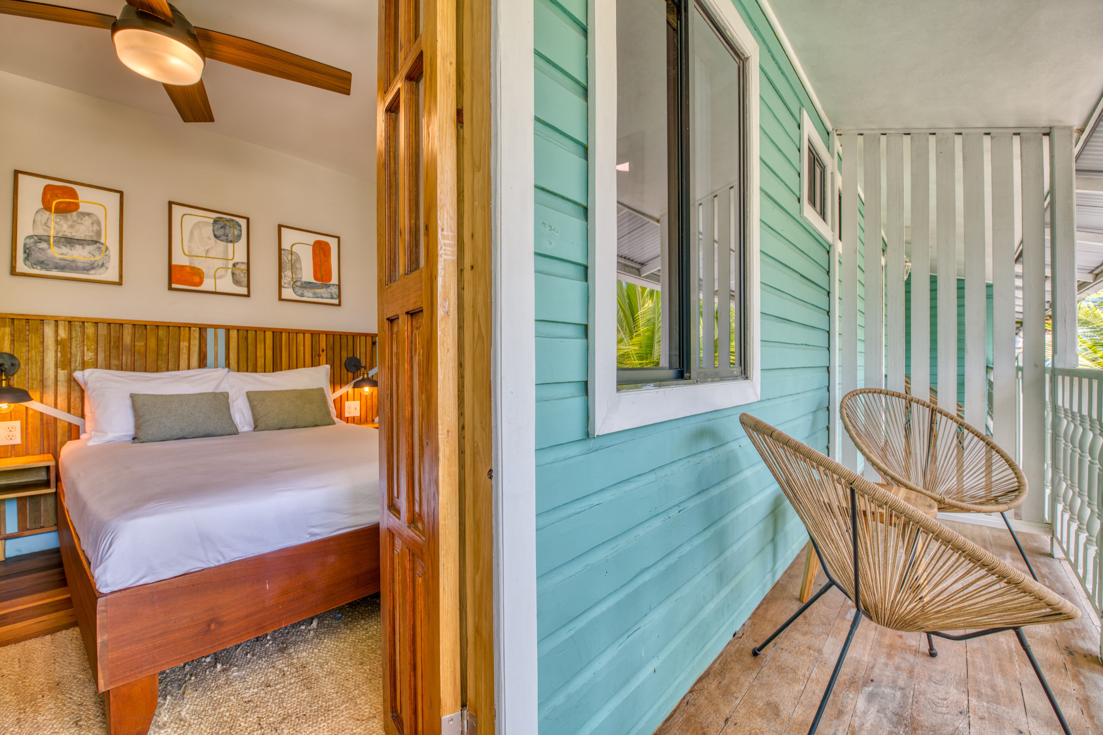 A bedroom with a wooden bed, a window, and a wicker chair on a porch.