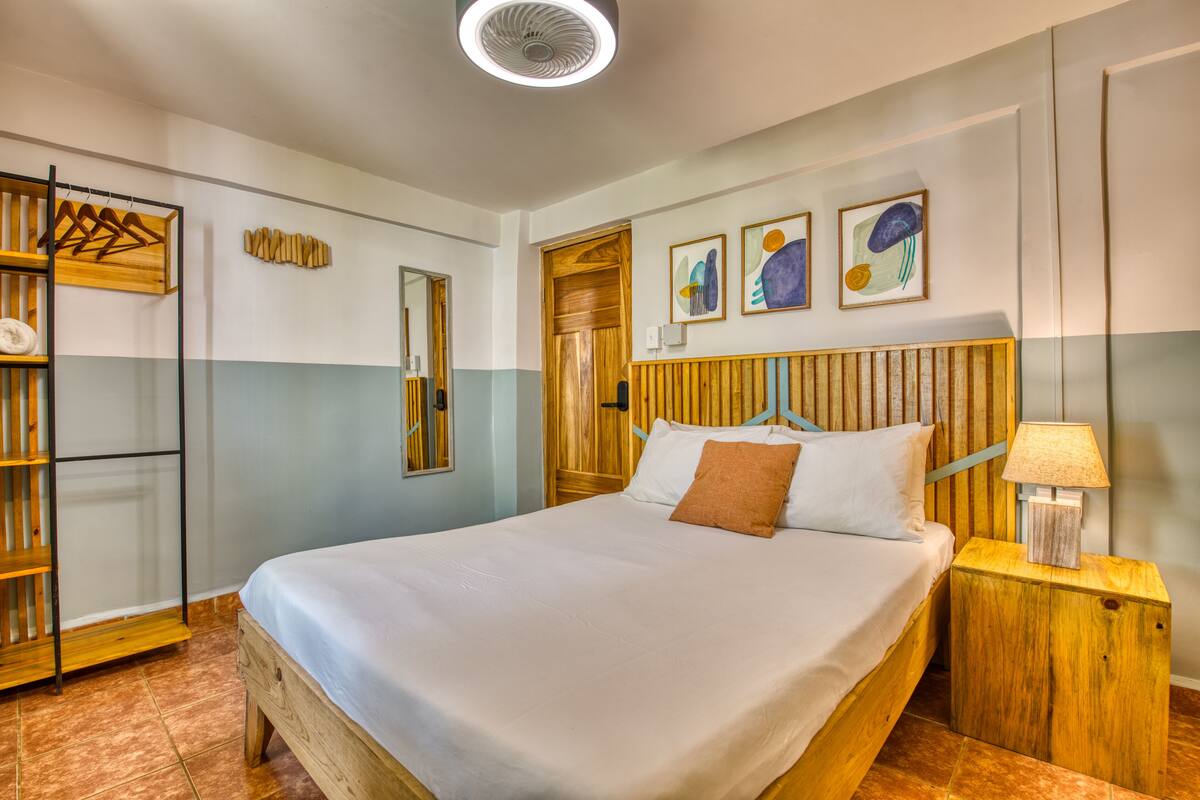 A neatly arranged bedroom with a wooden bed, a bedside table with a lamp, a wardrobe, and a mirror.