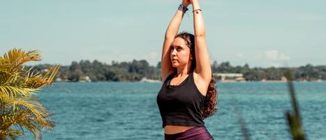 A person performing a yoga pose on a wooden dock by a body of water with a clear sky.