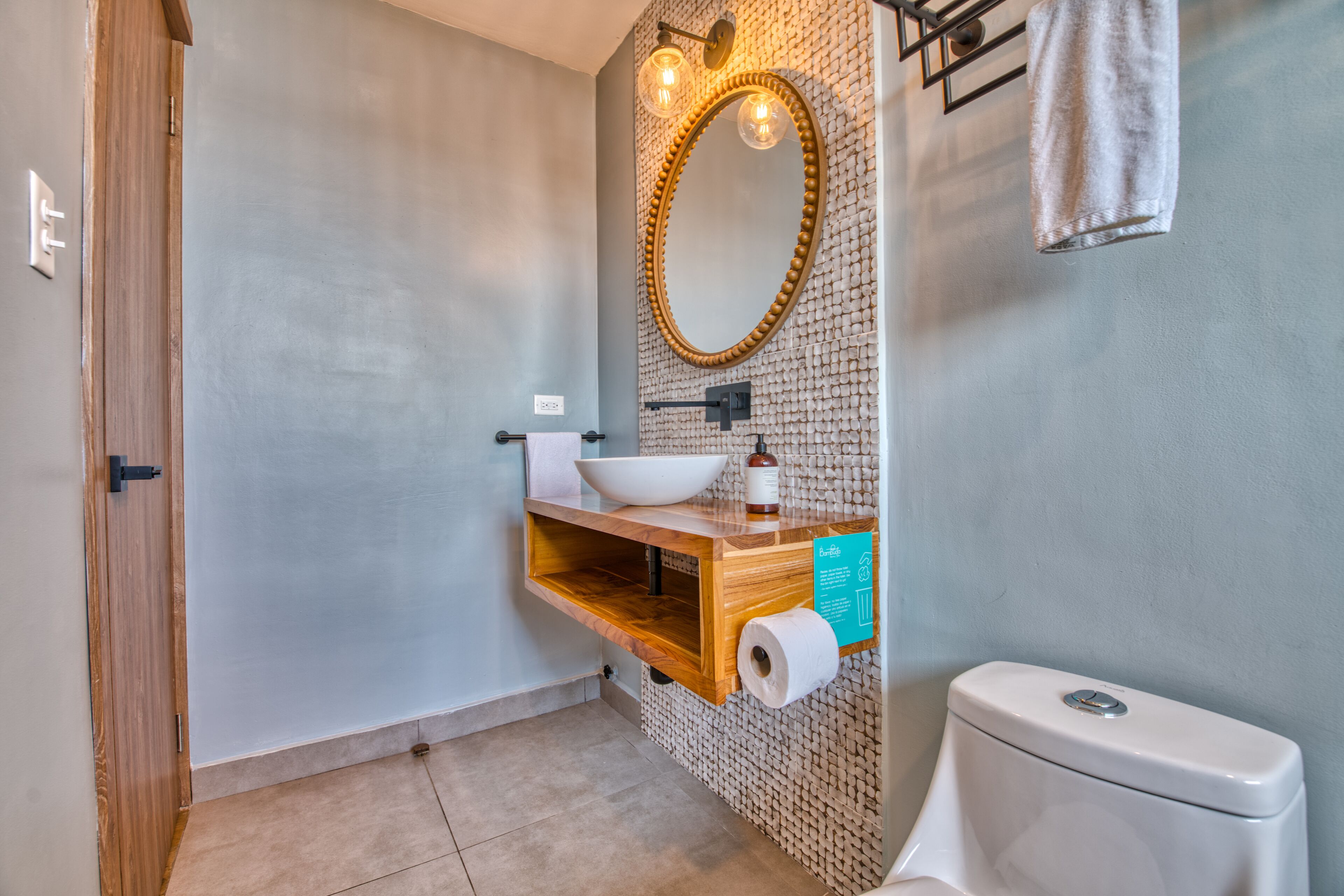 Un baño con tocador de madera, lavamanos blanco, espejo y retrete.