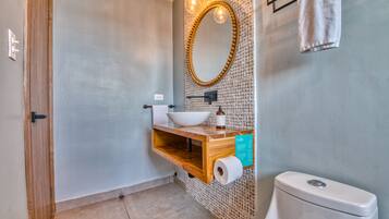A bathroom with a wooden vanity, a white sink, a mirror, and a toilet.