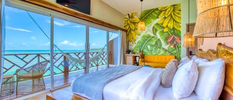 Un dormitorio con una cama grande, vista al océano, ventilador de techo y un mural temático tropical.