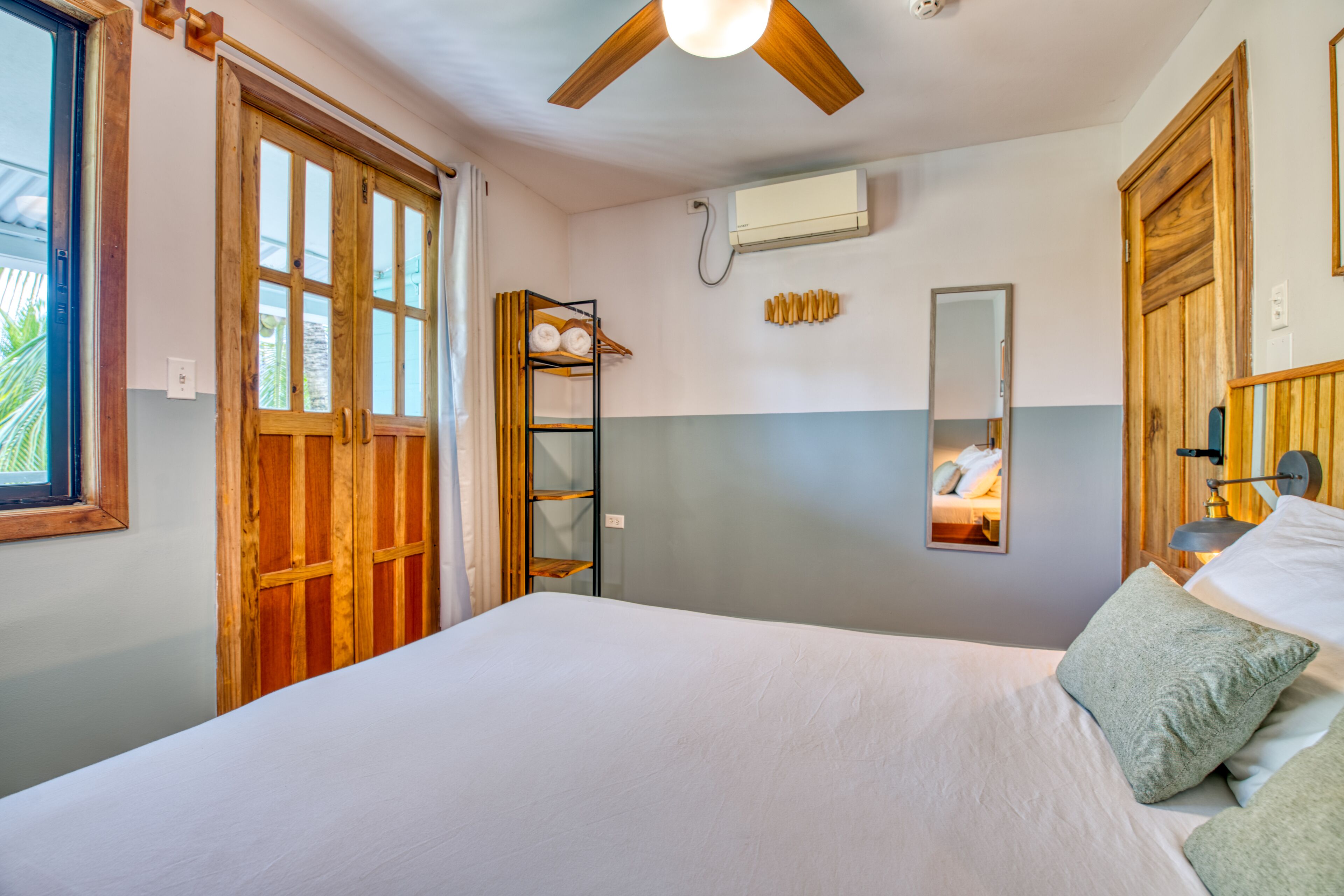 Un dormitorio con una cama grande, puertas de madera, ventilador de techo, aire acondicionado y un estante con toallas.