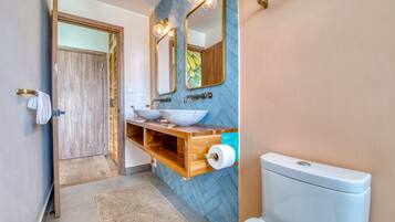Un baño con tocador de madera, dos espejos, un lavabo y un inodoro.