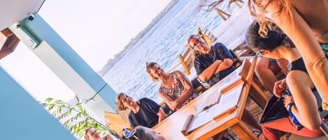 Un grupo de personas sentadas en una mesa de madera al aire libre, con vista al mar.