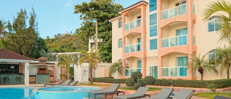 A hotel with a swimming pool, lounge chairs, and a bar area.
