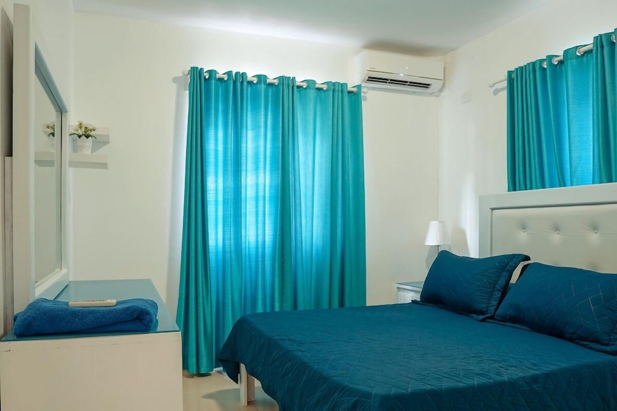 A hotel room with a bed, a bedside table, a lamp, and a window with curtains.