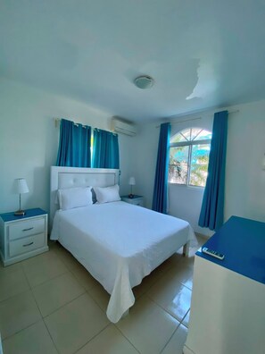 A bedroom with a bed, nightstands, a desk, and a window with curtains. - Ria Aparta Hotel (Puerto Plata)