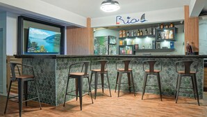 Un espace bar avec un mur recouvert de carreaux verts, un comptoir et quatre tabourets.