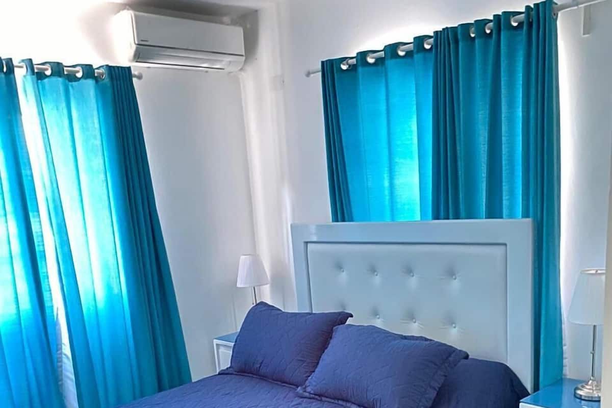 A bedroom with a bed, a nightstand, a lamp, and a window with curtains.