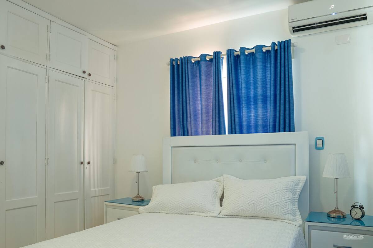 A bedroom with a bed, two bedside tables, a nightstand, a wardrobe, and a window with curtains.
