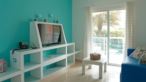 A living room with a white entertainment unit, a blue sofa, a small table, and a large window with curtains. - Ria Aparta Hotel (Puerto Plata)