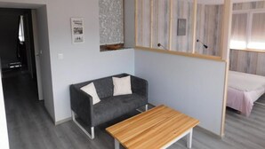 Una sala de estar moderna con un sofá gris, una mesa de centro de madera y una cama con colcha rosa.