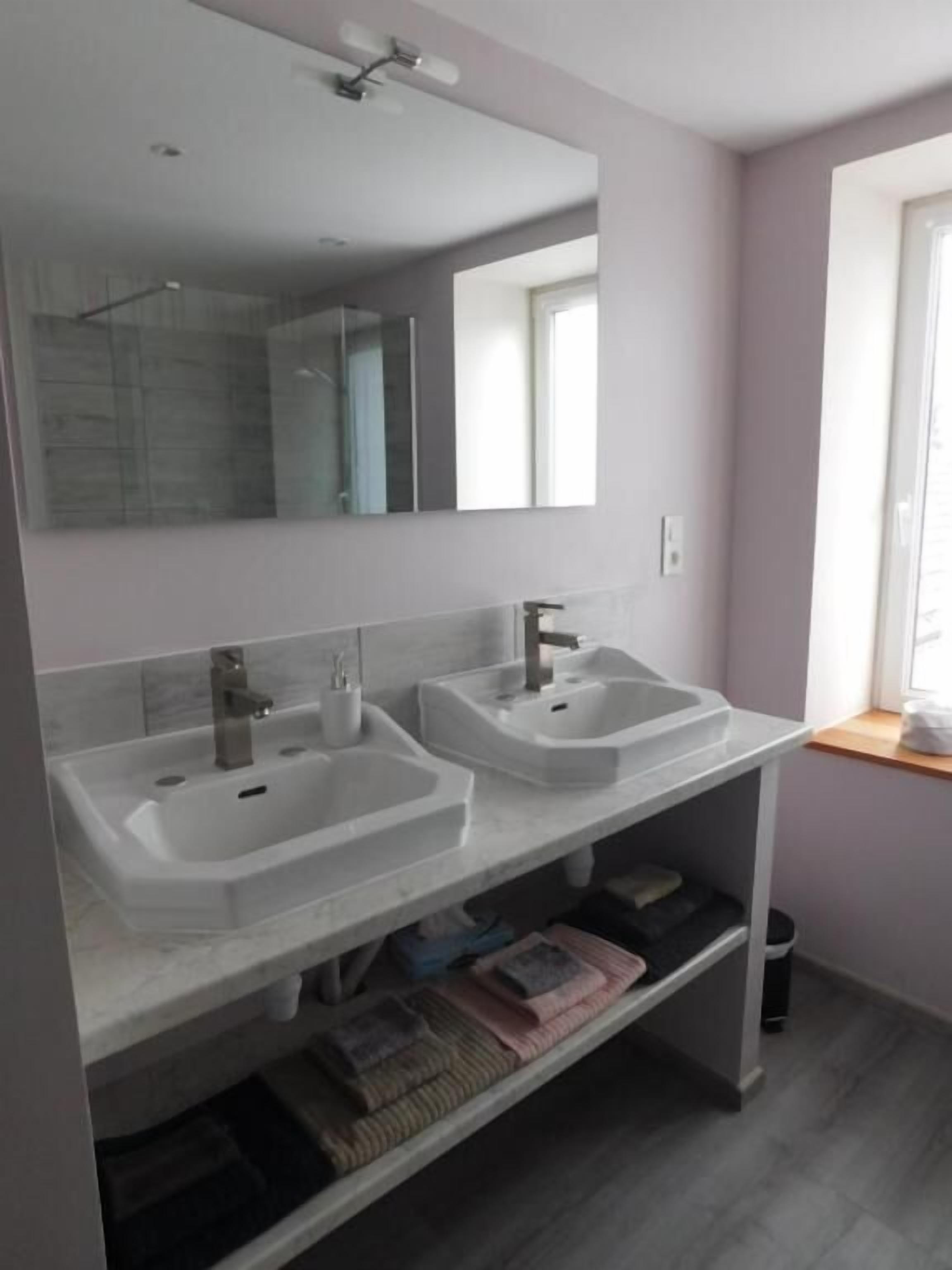 Un baño con dos lavabos, un espejo y una ventana.