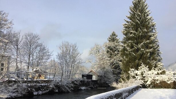 Orilla nevada de un río con una estructura de madera y árboles.