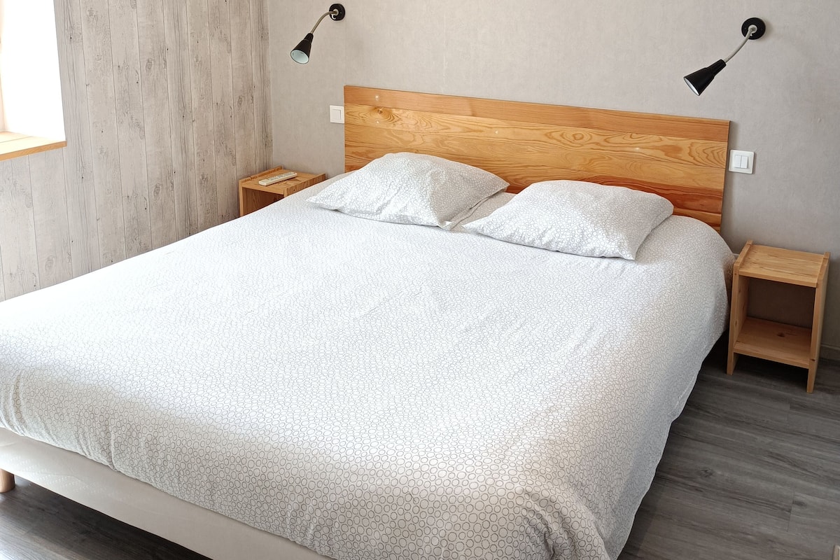 Un lit bien fait, avec une tête de lit en bois, deux tables de chevet et deux lampes fixées au mur.