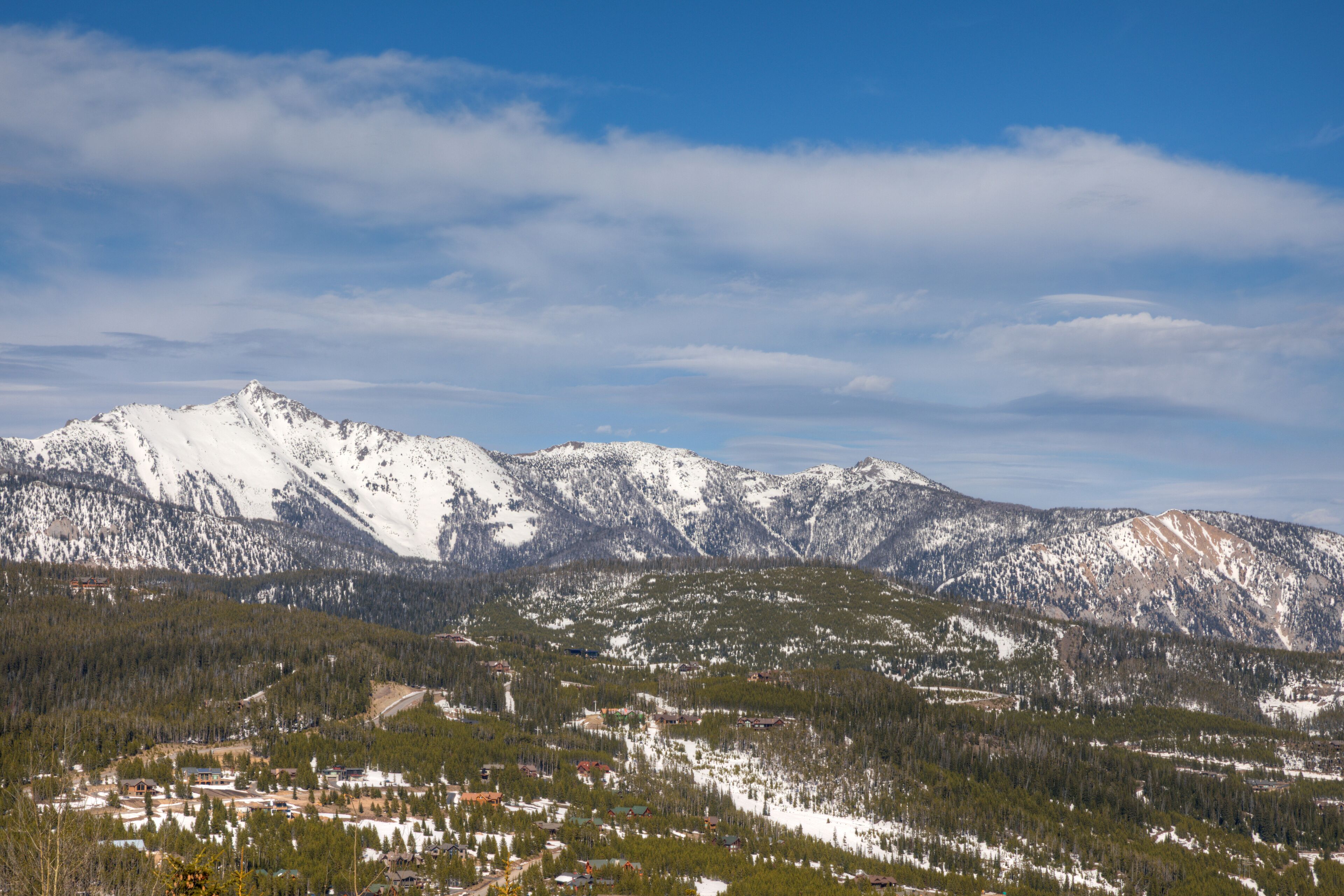 Paisagem montanhosa com picos cobertos de neve, uma cidade no vale com edifícios, e um céu claro.