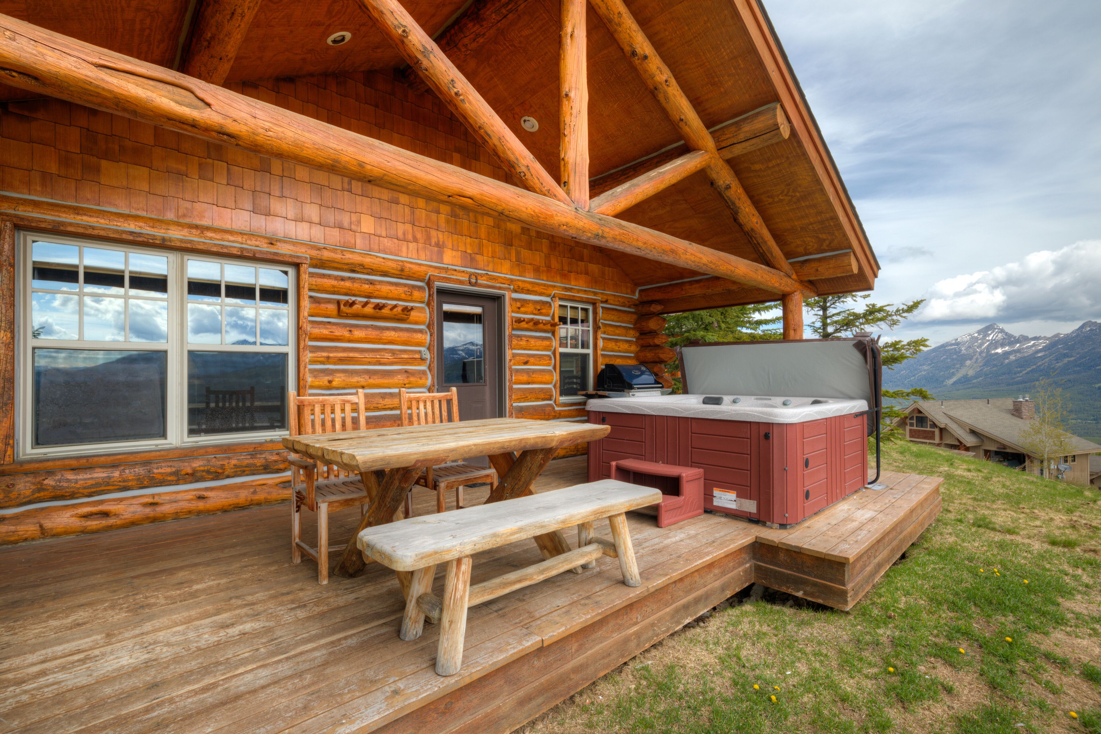 Een houten chalet met terras, een jacuzzi en uitzicht op de bergen.