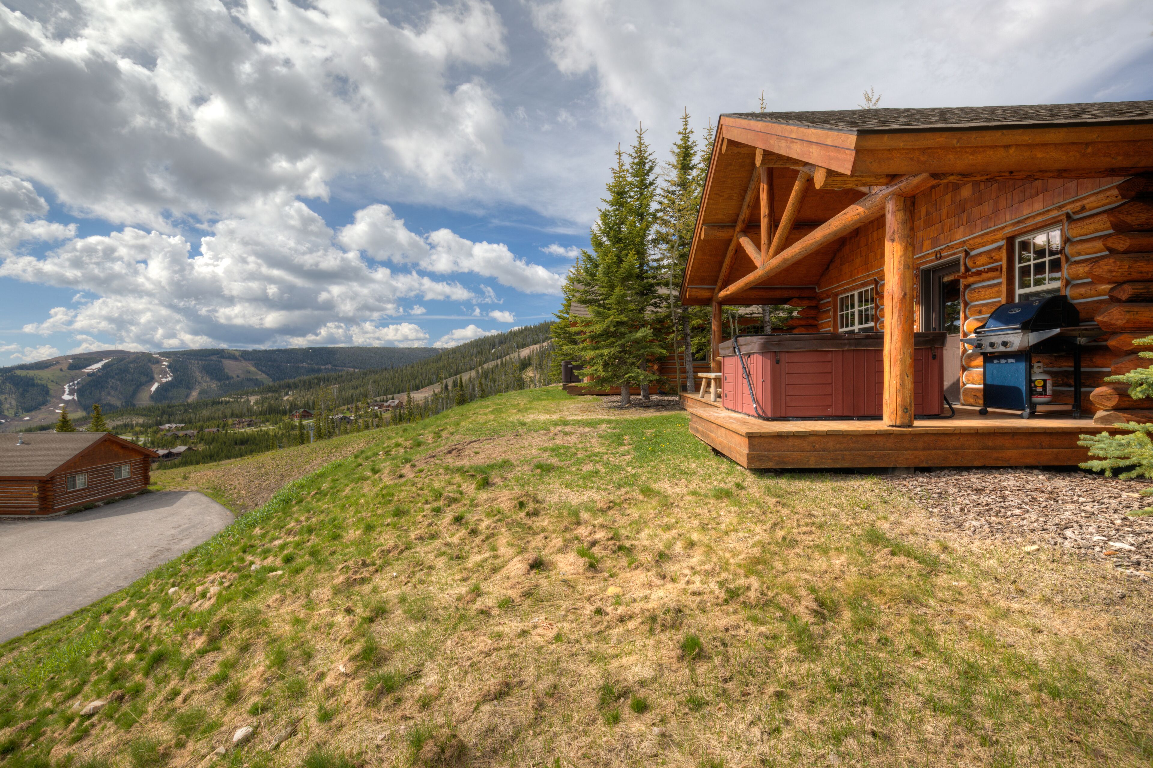A log cabin with a porch, a barbecue grill, and a view of mountains.