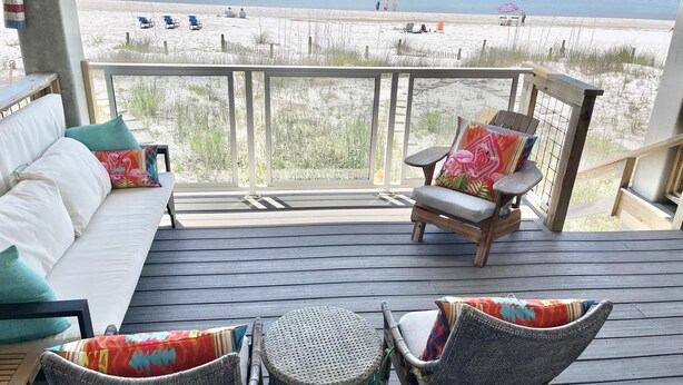 A deck with a sofa, wicker chairs, and a small table, overlooking a beach with people and umbrellas. - SEA SHANTY- Beachfront, Topnotch Comfort & Fully-Stocked! (Mexico Beach)