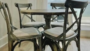 A dining area with a round table and four chairs, large windows with a view of the sky and clouds, and a wooden floor. - SEA SHANTY- Beachfront, Topnotch Comfort & Fully-Stocked! (Mexico Beach)
