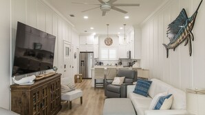 A spacious living room with a large flat-screen TV, a wooden cabinet, and a gray sofa with blue pillows. - SEA SHANTY- Beachfront, Topnotch Comfort & Fully-Stocked! (Mexico Beach)