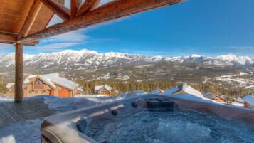 A hot tub with a view of snow-covered mountains and a wooden cabin in the background.