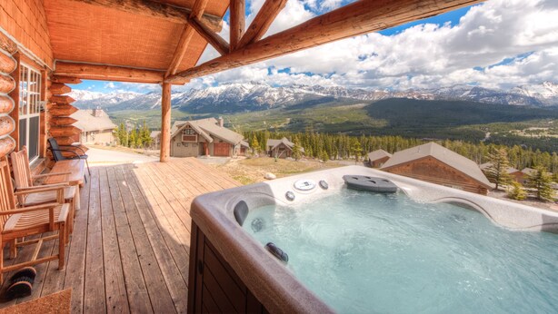 A wooden deck with a hot tub and chairs, overlooking a mountainous landscape.