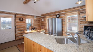 A kitchen with wooden walls, granite countertops, stainless steel appliances, and a view through the windows.