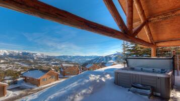 A wooden cabin with a hot tub and a view of snow-covered mountains.