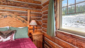 A log cabin room with a bed, a nightstand, a lamp, and a window with a snowy view.