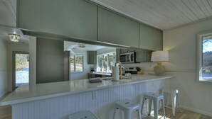 Una cocina moderna con encimera blanca, taburetes de bar y vistas al exterior.