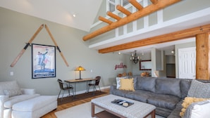 A spacious living room with a grey sofa, a wooden coffee table, and a dining area with a table and chairs. - Ski-In/Ski-Out Chalet | Lone Peak Views | Private Hot Tub (Big Sky)