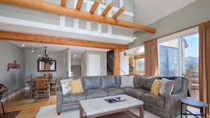 A spacious living room with a large sectional sofa, a wooden coffee table, and a dining area with a table and chairs. - Ski-In/Ski-Out Chalet | Lone Peak Views | Private Hot Tub (Big Sky)