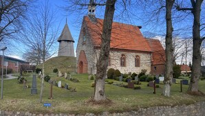 Una iglesia con techo rojo y una torre, rodeada por un cementerio con lápidas.