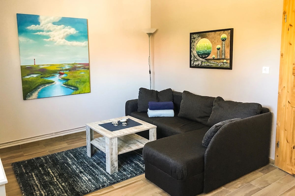 Un salon avec un canapé gris foncé, une petite table basse en bois et un tableau représentant un paysage avec un phare.