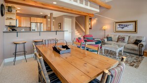 A spacious living area with a wooden dining table, comfortable seating, a kitchen with modern appliances, and a staircase leading to an upper level. - Ski-in/ski-out home w/private hot tub in Moonlight Basin - Saddle Ridge - Montana Mountain Chalet (Big Sky)