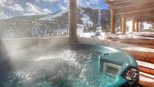 Un jacuzzi con vistas a montañas nevadas y un telesilla al fondo.