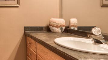 A bathroom with a marble countertop, wooden cabinets, a sink, and a mirror.