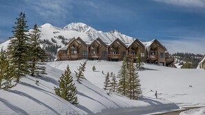 Un chalet doté de plusieurs cabanes en rondins, une montagne enneigée en arrière-plan et un ciel dégagé.