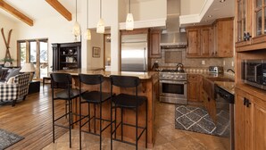 Una cocina amplia con armarios de madera, un refrigerador de acero inoxidable, un horno y un microondas. Hay tres taburetes negros en la isla.