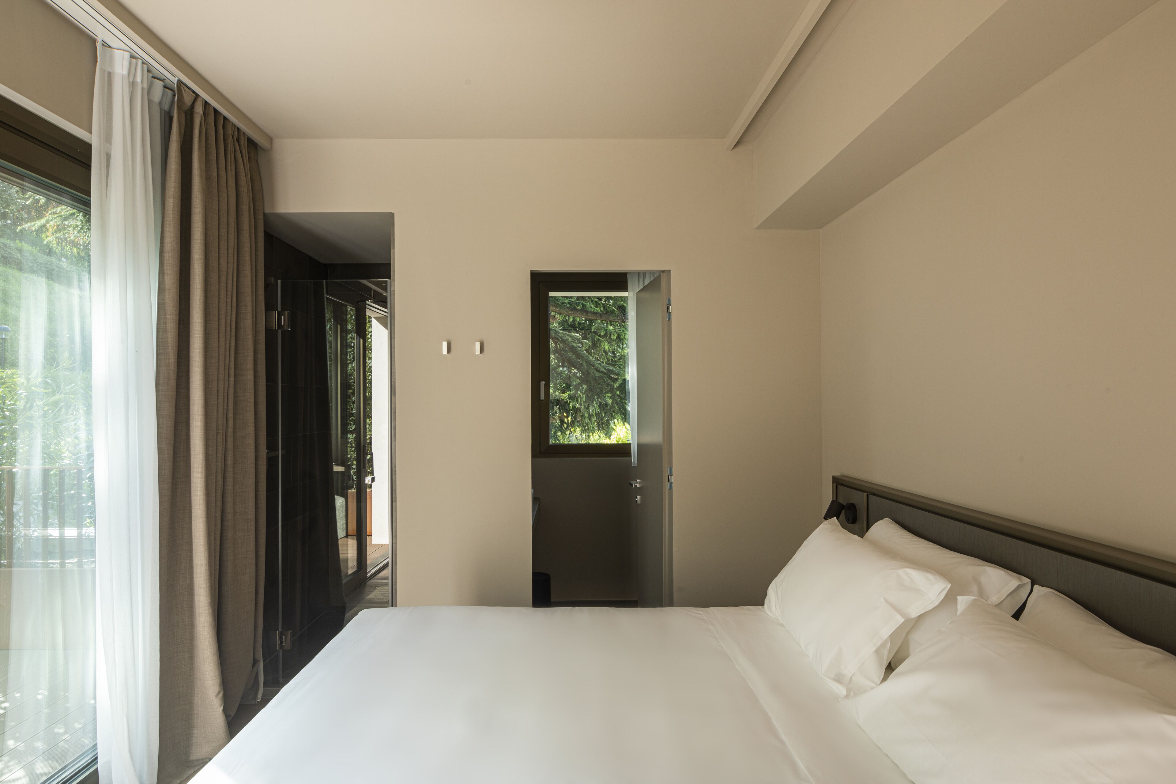 A hotel room with a large bed, a window with curtains, and a door leading to a balcony.