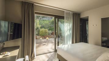 A hotel room with a bed, a TV, a desk with a chair, and a balcony with outdoor seating.
