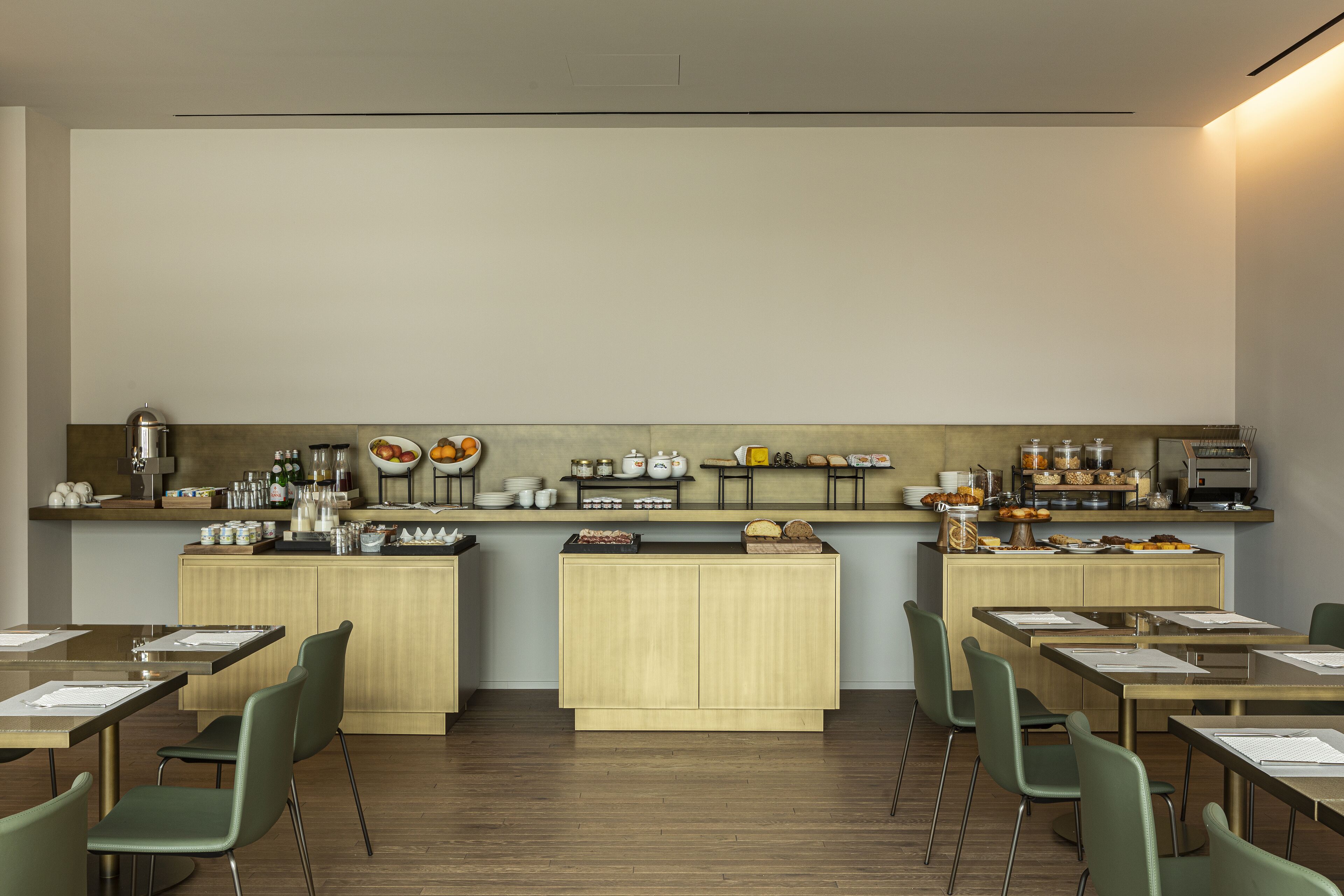 A modern dining area with wooden tables and chairs, a kitchen counter with various food items, and a clean, minimalist design.