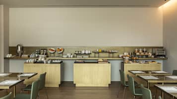 A modern dining area with wooden tables and chairs, a kitchen counter with various food items, and a clean, minimalist design.