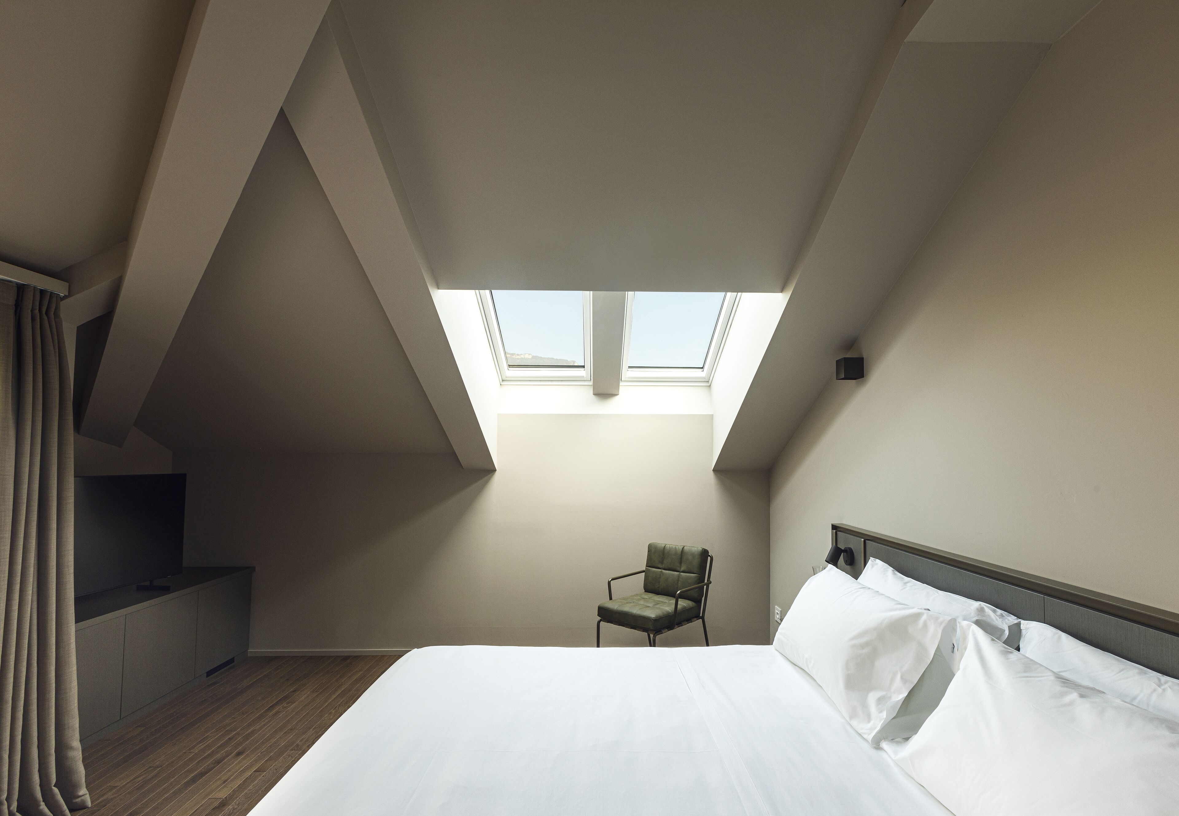 Une chambre avec un puits de lumière, un lit, une chaise et un petit escalier.