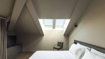 A bedroom with a skylight, a bed, a chair, and a small staircase.