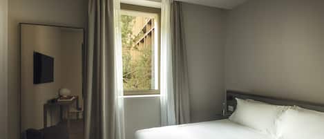 A bedroom with a large bed, a bedside table with a lamp, a chair, and a window with curtains.