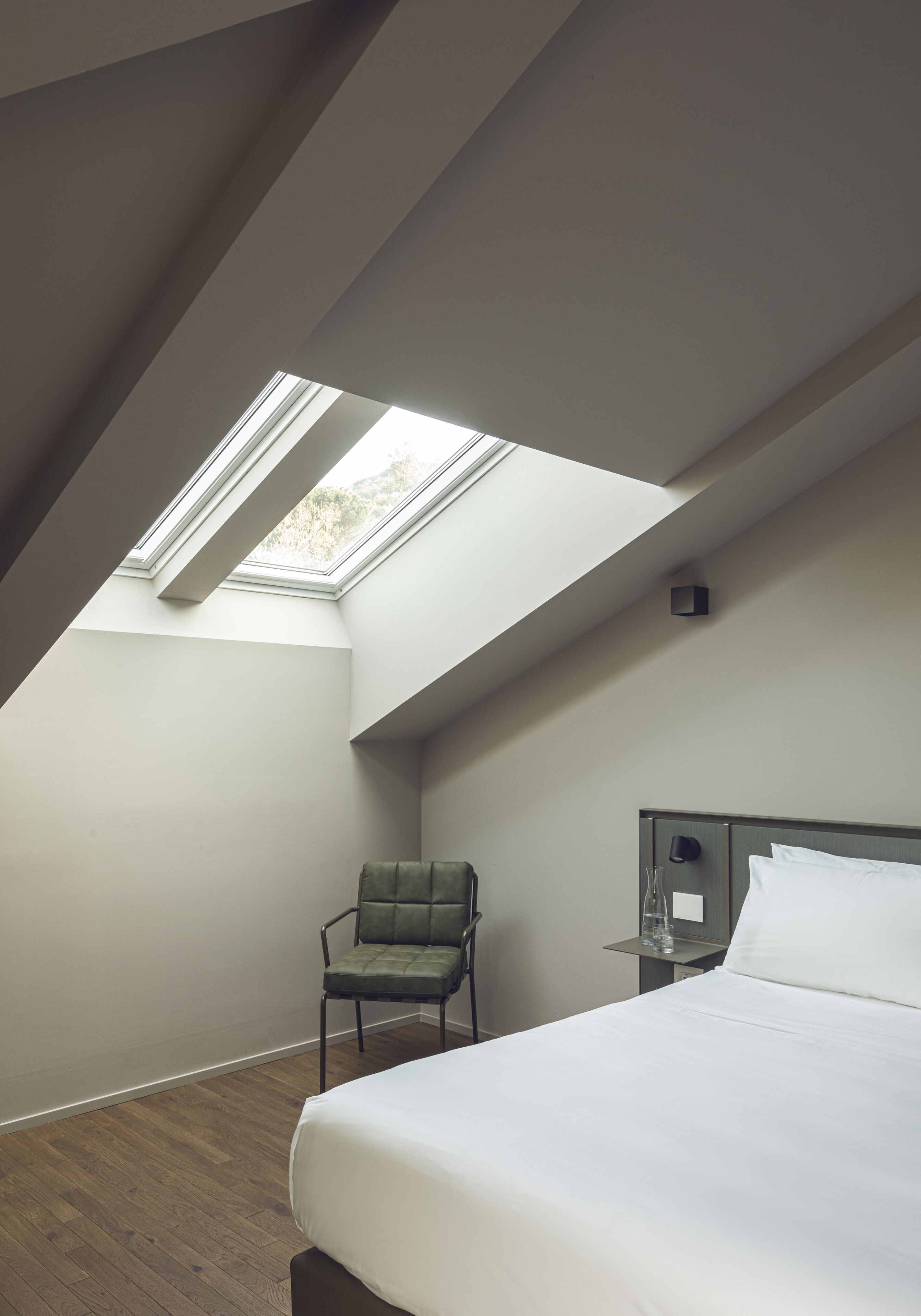 A bedroom with a skylight, a bed, a chair, and a bedside table.
